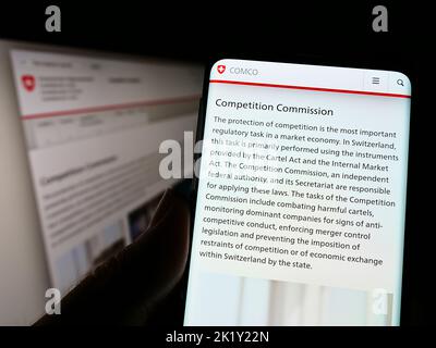 Person holding cellphone with web page of competition commission Wettbewerbskommission (Weko) on screen. Focus on center of phone display. Stock Photo
