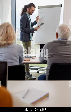 A teacher is teaching a lesson small group of senior students while writing on a table and looking at the tablet. Stock Photo