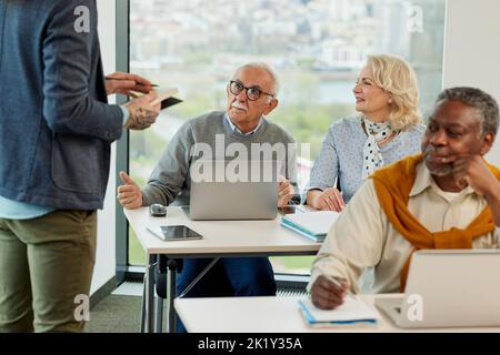 A group of senior students sit in a classroom with their teacher and work on a school project. Stock Photo