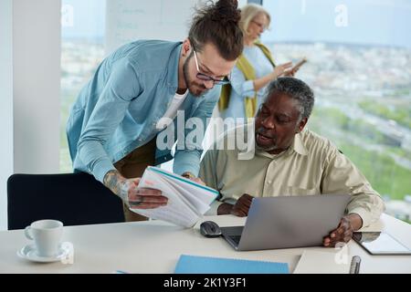 A young teacher explaining to senior student how do computer programming on a laptop. Stock Photo