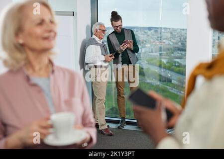 Senior students having a break between lectures. A tutor showing something interesting on a phone to a senior man. Stock Photo