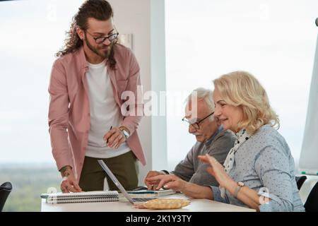 A young professor is checking on senior students who is using laptops in a classroom. Stock Photo