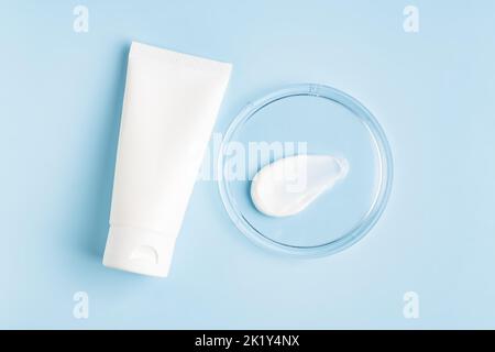 Natural cosmetic laboratory concept. Petri dish with cosmetic cream, white cream tube on blue background top view, mockup Stock Photo
