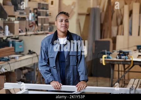 Waist up portrait of female worker standing in factory workshop and looking at camera, copy space Stock Photo
