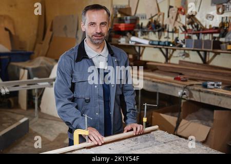 Waist up portrait of mature male worker looking at camera while working with wood in in factory workshop, copy space Stock Photo