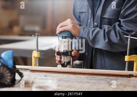Closeup of unrecognizable male worker cutting wood with power tool in factory workshop, copy space Stock Photo