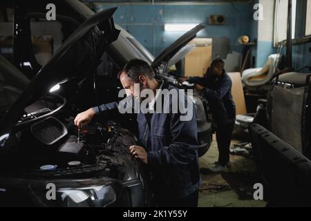 Side view portrait of two mechanics fixing trucks in garage workshop, copy space Stock Photo