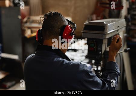 Back view of worker operating machine units in industrial workshop and wearing protective gear Stock Photo