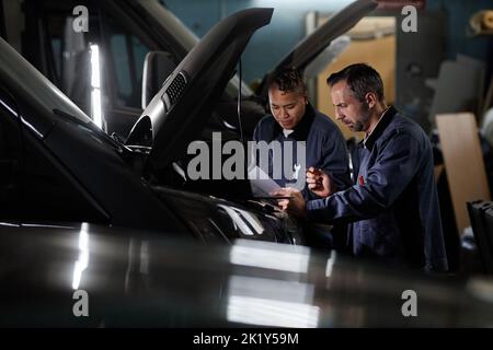 Side view portrait of two mechanics using laptop during car checkup in garage with accent light, copy space Stock Photo