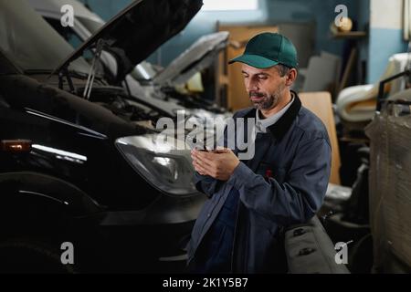 Waist up portrait of mature male worker using smartphone in at car factory workshop Stock Photo