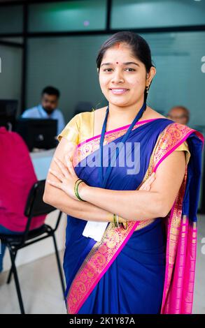 vertical shot Happy confident bank employee standing with arms crossed by looking camera at office - concept of successful career, leadership and Stock Photo