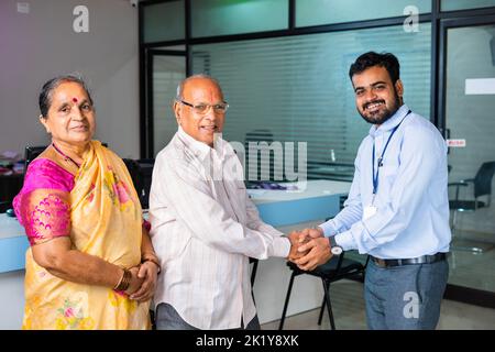 Happy smiling banker greeting by shaking hand to senior couple at bank - concept of financial support, banking adviser and consultation. Stock Photo