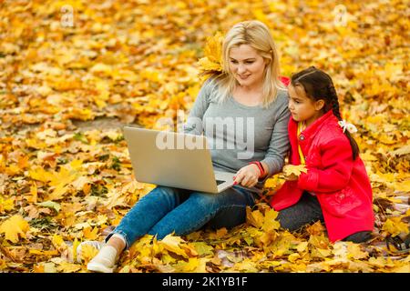 Happy mother and her tdaughter using laptop in the park. Stock Photo