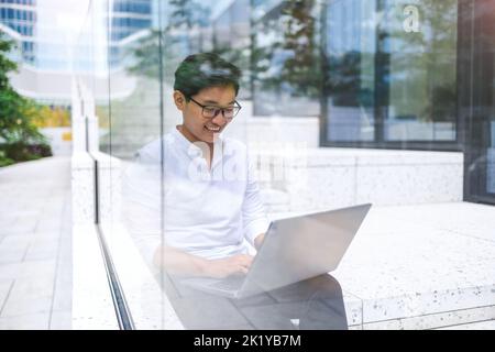 Young businessman sitting outdoors in the city working on laptop Stock Photo
