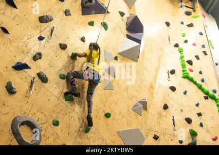 bouldering, little girl climbing up the wall and climber multicolored grips. Leisure activity Stock Photo