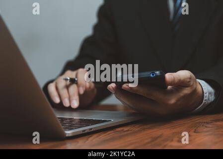 Businessman working with smartphone in his hands and computer laptop on desk. Stock Photo