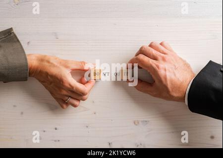 Hands of male and female business people assembling a Dont quit Do it sign written on wooden blocks and wooden background. Stock Photo