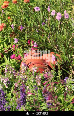 Bright red fire hydrant standing in the summer flower garden. Stock Photo