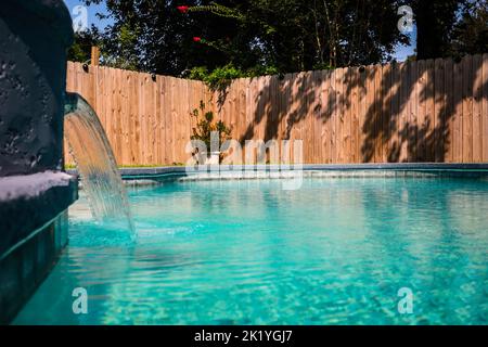 Close up of a gray grey accent swimming pool with turquoise blue water in a fenced in backyard in a suburb neighborhood Stock Photo