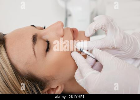 Beautician doing injection into nasolabial folds to female patient. Correction of wrinkles on woman face using dermal fillers Stock Photo