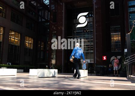 A businessman walks towards Scotia Plaza in downtown Toronto; the Scotiabank logo is seen illuminated in the shade, as the sun glares down. Stock Photo