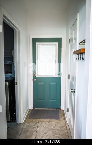 A dark teal painted interior back door inside an Acadian style Louisiana home with tile floors and hooks to hang jackets on the wall Stock Photo