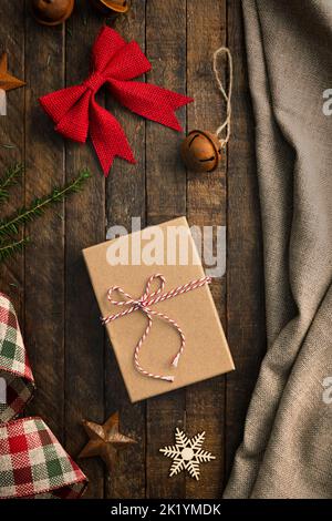 Rustic Christmas scene form top view with gift in the center and canvas, burlap and rusted metal items on wooden table. Stock Photo