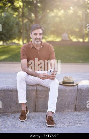 Man looking away and relaxing while using a mobile phone outdoors in a park. Technology concept. Stock Photo