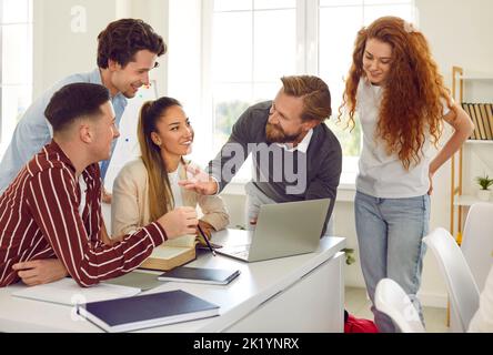Teacher talking and using laptop at class working on project with his teenage students. Stock Photo