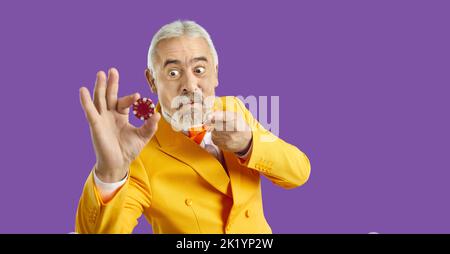 Portrait of funny crazy angry senior casino gambler in yellow suit holding poker chip Stock Photo