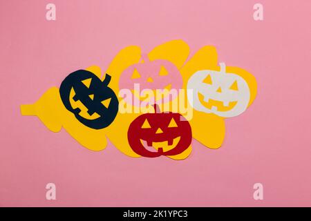 yellow paper oak leaf, colorful paper carved pumpkin on it, creative halloween concept, flat lay, paper craft, pink background Stock Photo