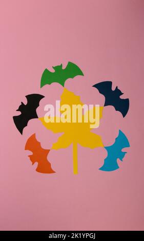 yellow maple leaf on a pink background, colorful bats come out of the leaf, creative halloween concept, flat lay, paper craft Stock Photo