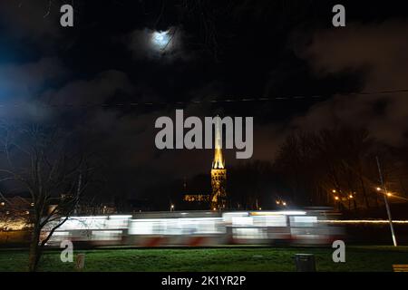 Tallinn, Estonia -  January 4, 2020: night scenic view of a train passing with St. Olaf’s Church in the background Stock Photo