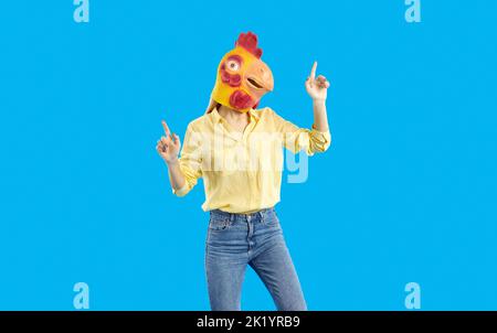 Young girl wearing funny yellow chicken mask dancing isolated on blue background Stock Photo
