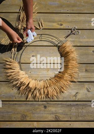 Parts of woman hands with hot glue making wheat door wreath Stock Photo
