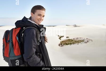 She enjoys a good hike. Portrait of a young female hiker walking along the sand dunes. Stock Photo