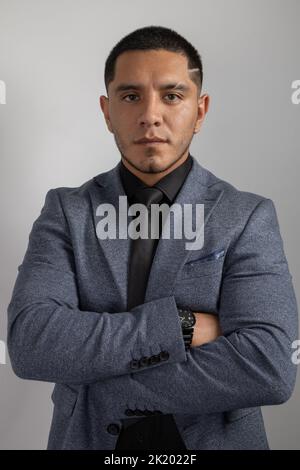 young latin man with short hair wears formal clothes, a suit, shirt and tie, study details of the face, business person with arms crossed Stock Photo