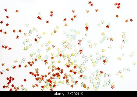 Many small red, green and blue shimmering decorative shiny stars shining on a white surface. View from above. Concept of celebrating Christmas or other holiday. Copy space for text. Stock Photo
