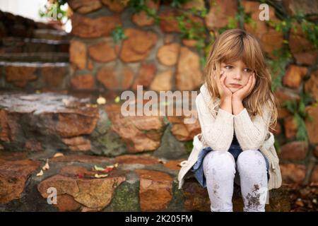 Loneliness strikes. A cute little girl looking lonely while sitting outside on an autumn day. Stock Photo