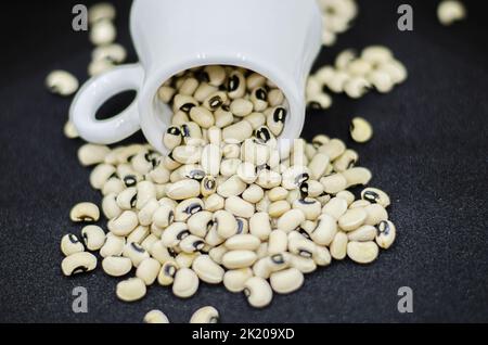 Black eyed beans pouring from a mug on a black background,  dried kidney beans on a black background Stock Photo