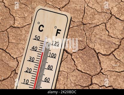 wooden thermometer shows hot temperature on dried cracked brown earth texture Stock Photo
