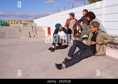 Taking a break from the boards. a group of friends hanging out at a skate park. Stock Photo