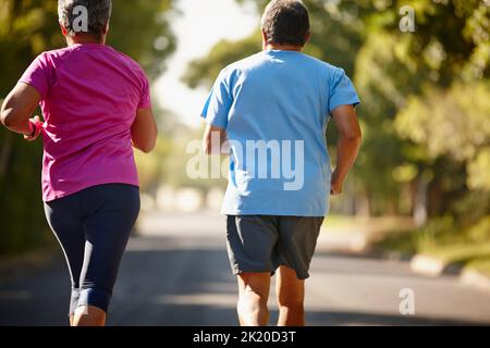We keep each other exercising. Rearview shot of a mature couple jogging together on a sunny day. Stock Photo