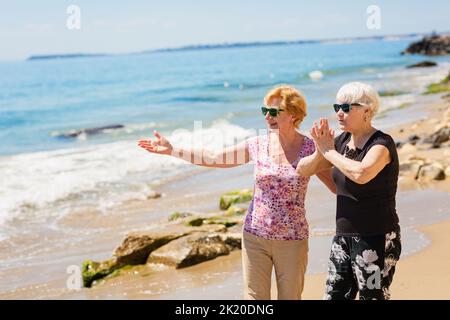 Two senior women are walking along the rocky shore, talking and laughing Stock Photo