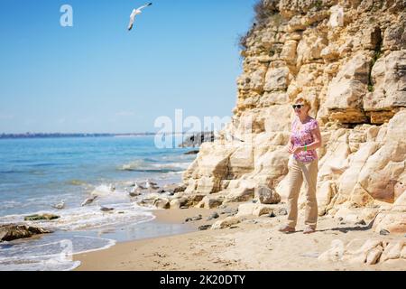 Elderly woman in sunglasses feeds seagulls on the beach Stock Photo
