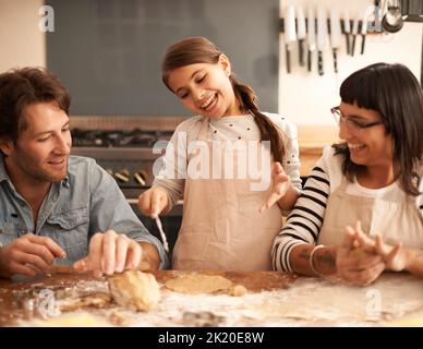 We should make some gingerbread women too. a family having fun baking in a kitchen. Stock Photo