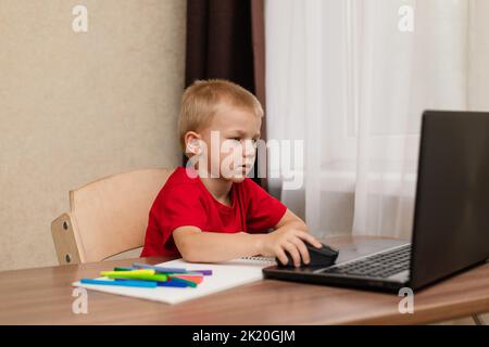 Online distance learning. The child looks carefully at the laptop and studies the drawing lesson online on the Internet. Online school. Stock Photo