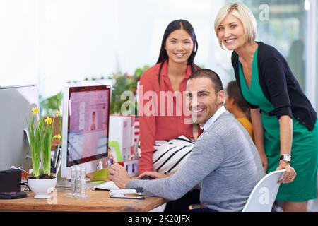 Working together to get the job done. Portrait of three coworkers working around a single computer. Stock Photo
