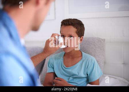 Take a deep breath in. a caring father giving his son an asthma pump at home. Stock Photo