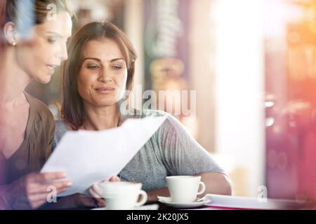 Quickly reviewing some paperwork over coffee. Two women discussing paperwork during a business meeting at a cafe. Stock Photo